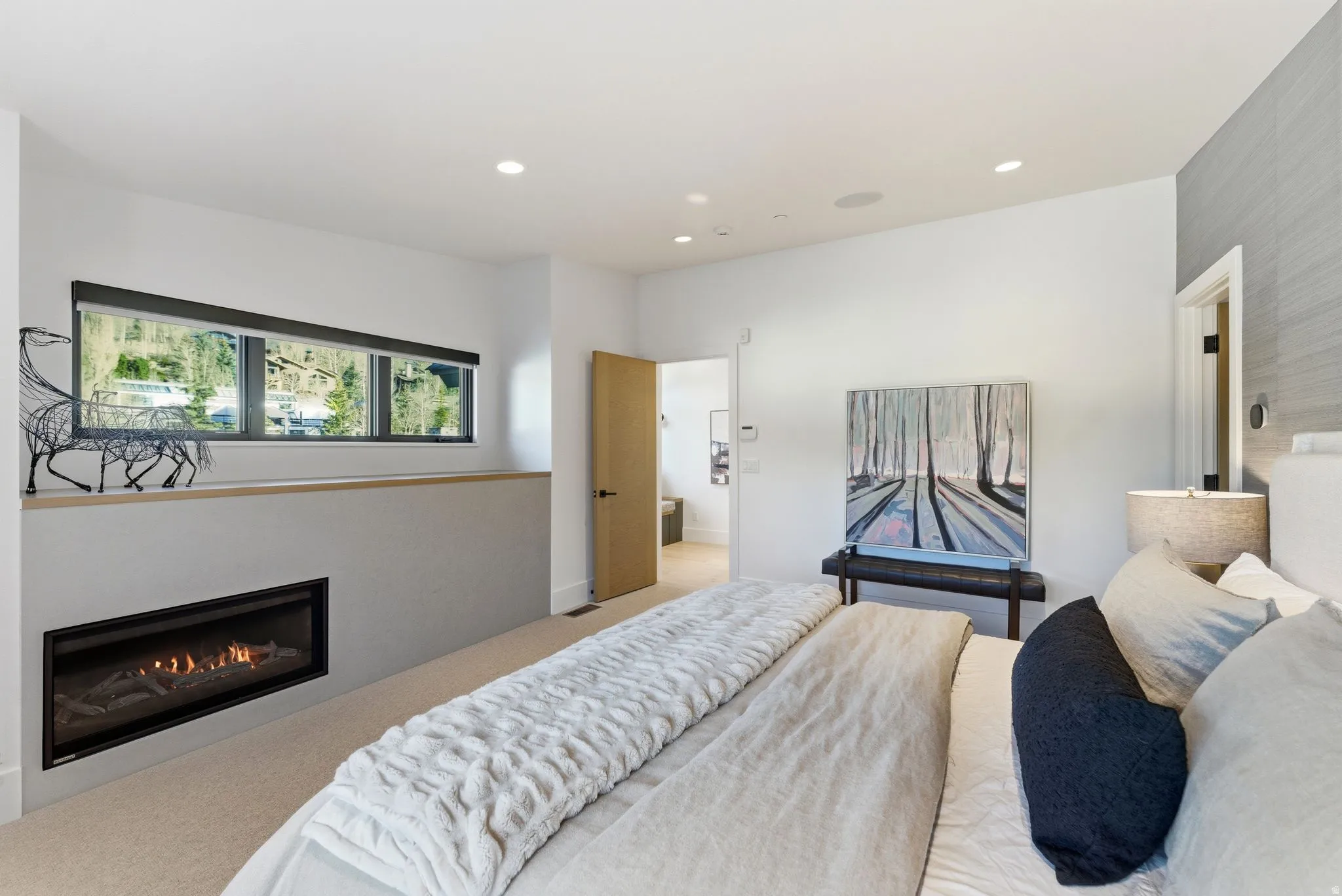 Carpeted bedroom featuring a glass covered fireplace, recessed lighting, and connected bathroom