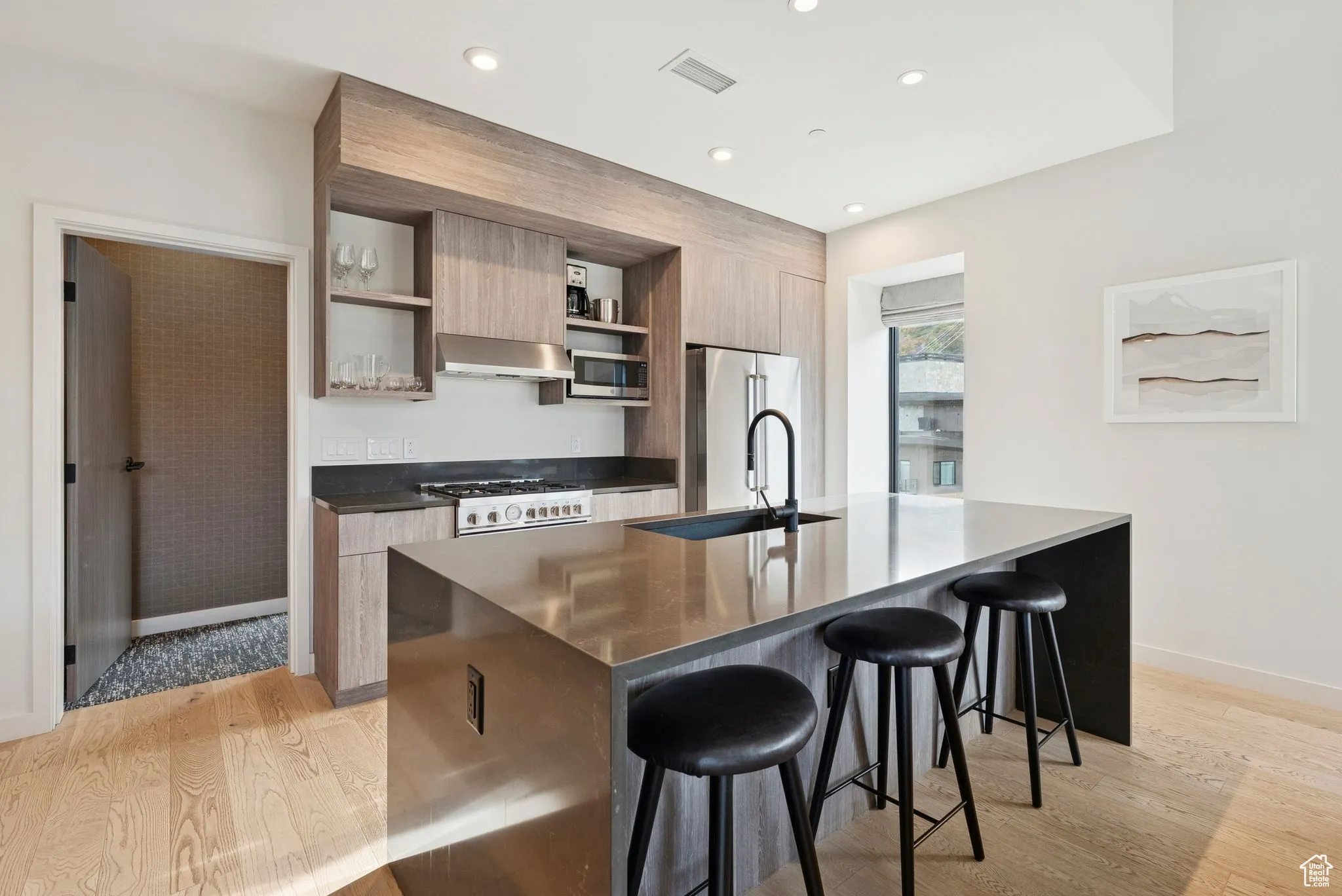 Kitchen with a kitchen breakfast bar, light wood-style flooring, open shelves, dark stone counters, and stainless steel appliances