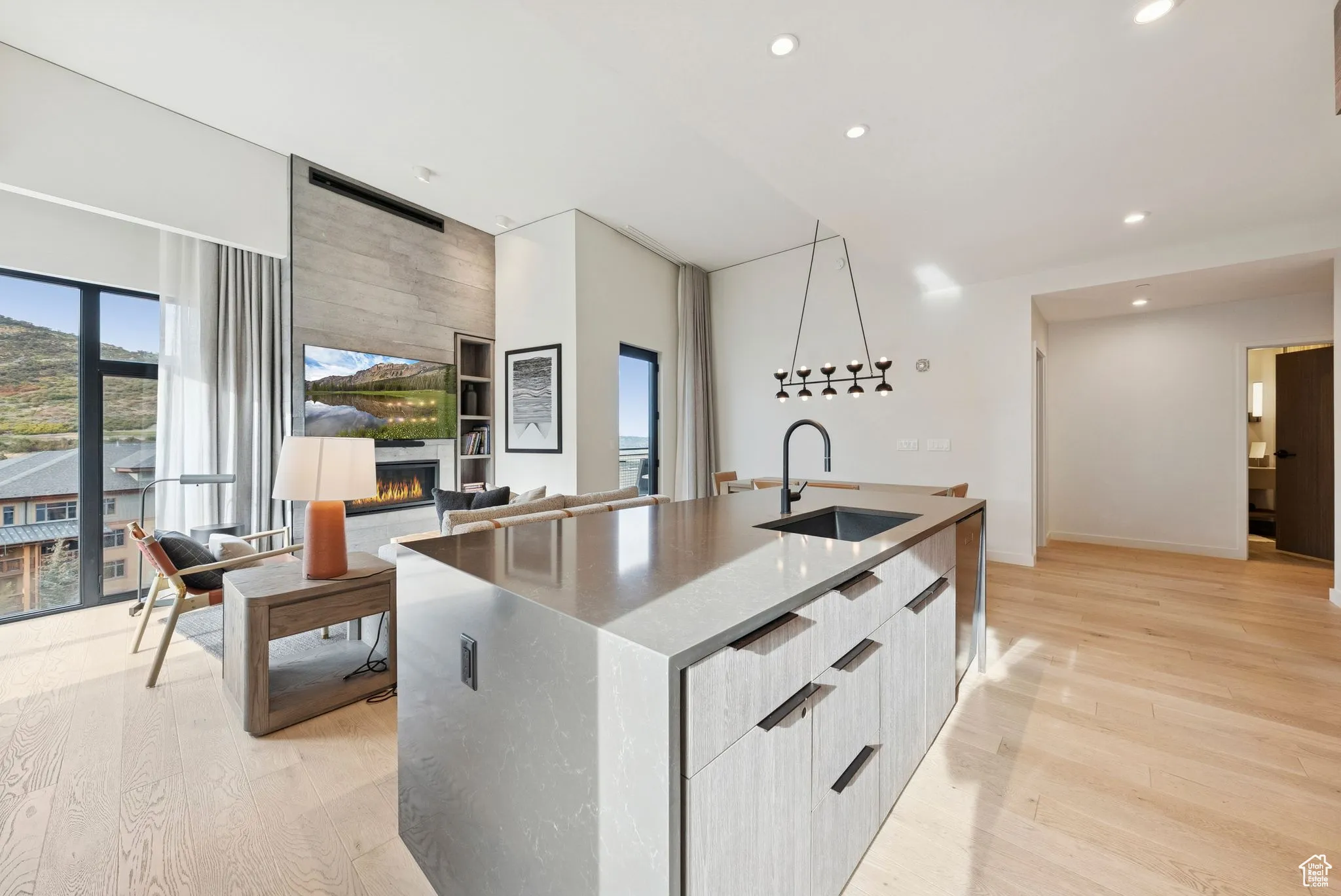 Kitchen featuring modern cabinets, light wood-style flooring, a large fireplace, a center island with sink, and recessed lighting