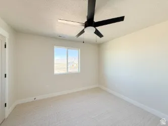 Empty room featuring a textured ceiling, light colored carpet, and ceiling fan