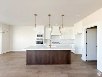 Kitchen with white cabinetry, hanging light fixtures, a center island with sink, and custom range hood