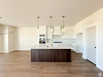 Kitchen featuring light countertops, dark brown cabinets, light wood-style floors, white cabinetry, and a center island with sink