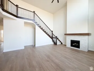 Unfurnished living room featuring a high ceiling, stairs, a fireplace, wood finished floors, and a ceiling fan