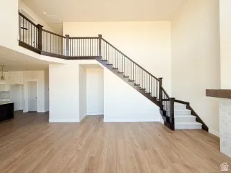 Unfurnished living room featuring stairs, light wood-type flooring, and a towering ceiling