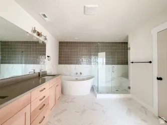 Full bath with double vanity, a marble finish shower, a freestanding bath, and tile walls