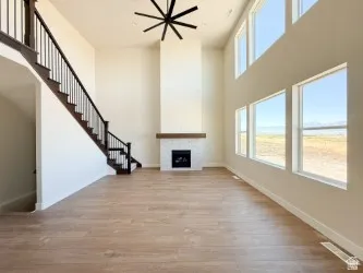 Unfurnished living room featuring plenty of natural light, a fireplace, light wood-style flooring, stairway, and a towering ceiling