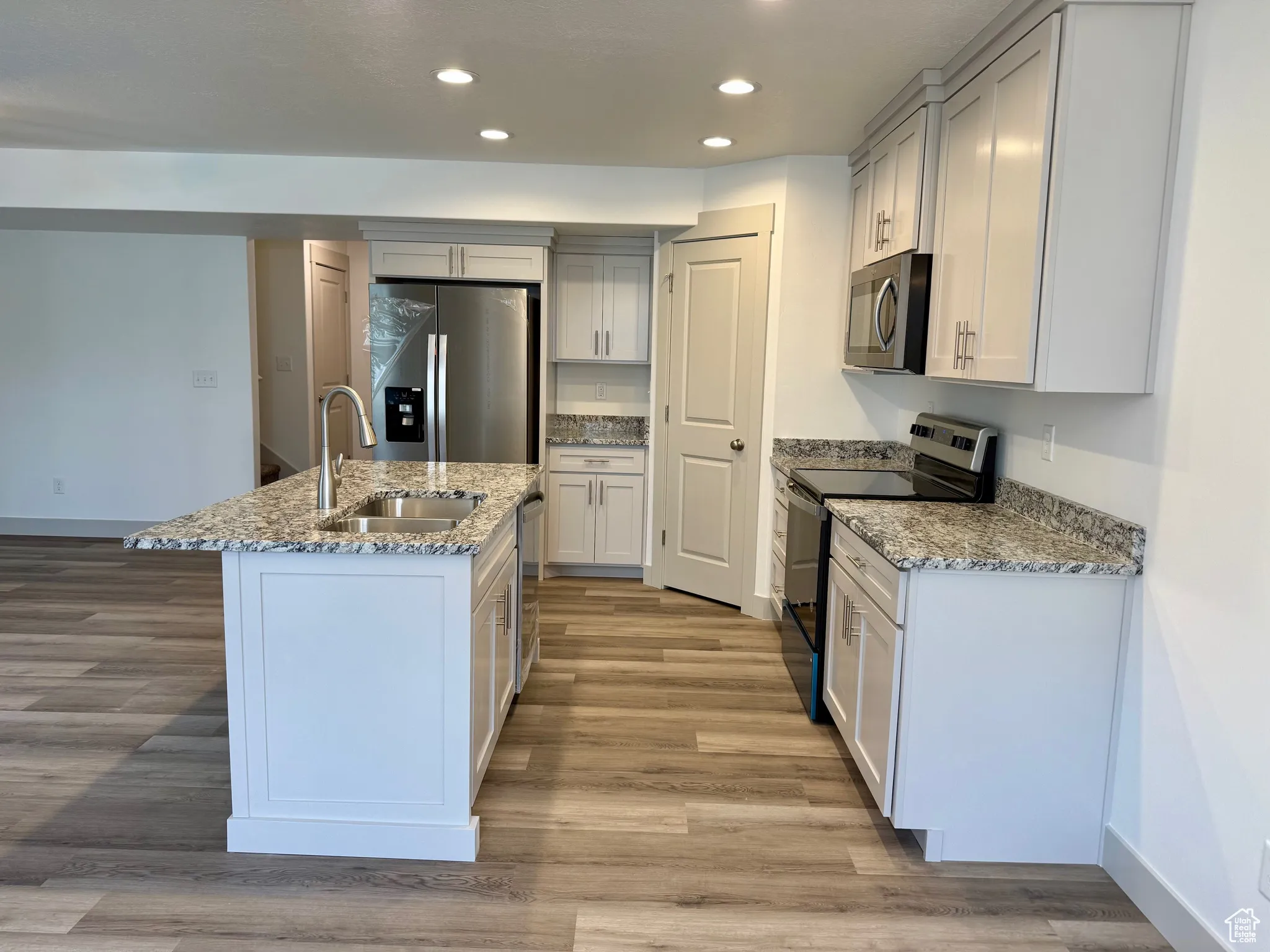 Kitchen featuring light stone counters, stainless steel appliances, recessed lighting, a kitchen island with sink, and light wood-style flooring