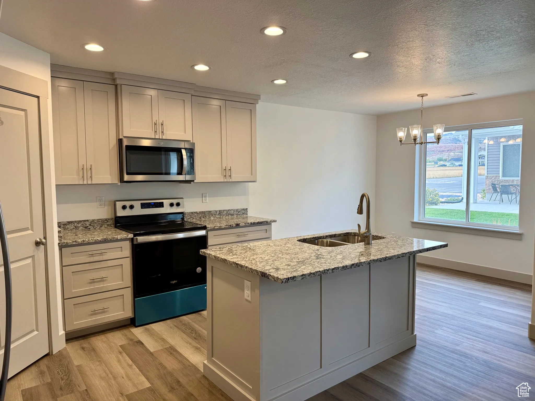 Kitchen featuring stainless steel appliances, light stone countertops, recessed lighting, light wood-style floors, and hanging light fixtures