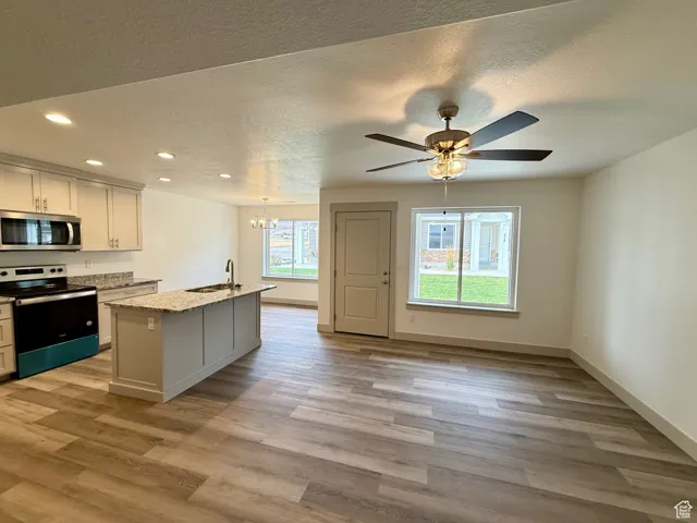Kitchen featuring stainless steel appliances, a chandelier, a center island with sink, light stone countertops, and recessed lighting