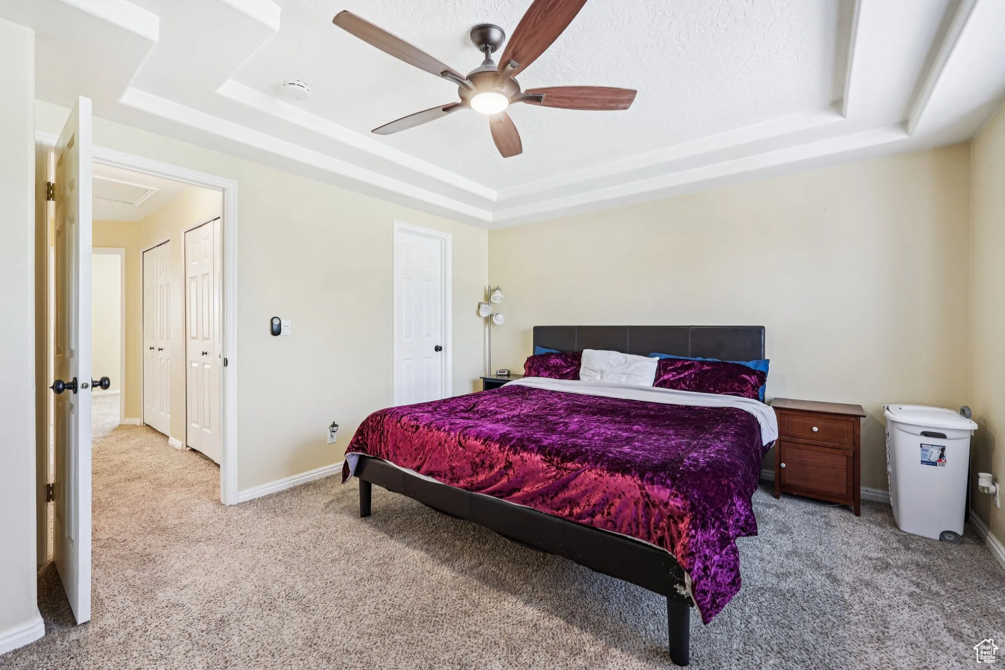Bedroom with a tray ceiling, light colored carpet, a ceiling fan, and a textured ceiling