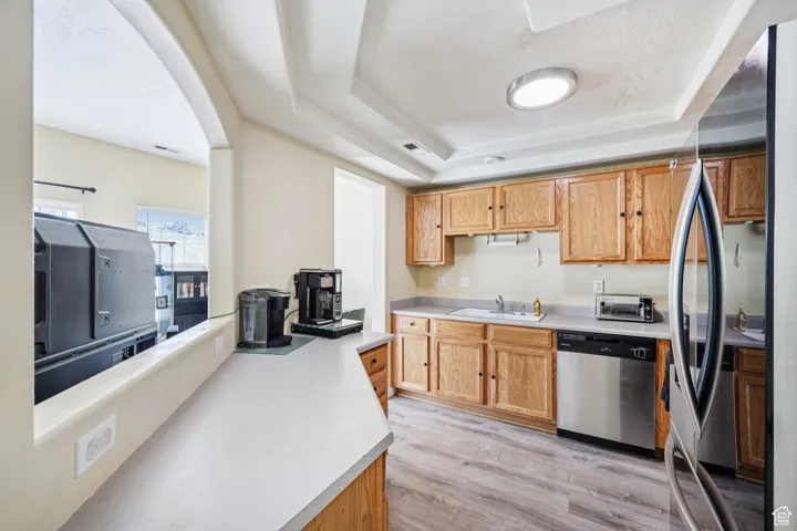 Kitchen featuring a raised ceiling, light countertops, stainless steel appliances, light wood-style flooring, and arched walkways