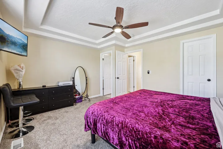 Bedroom with a raised ceiling, a textured ceiling, carpet flooring, and ceiling fan
