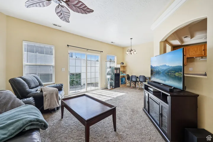 Living room featuring light carpet, a chandelier, a textured ceiling, and a ceiling fan