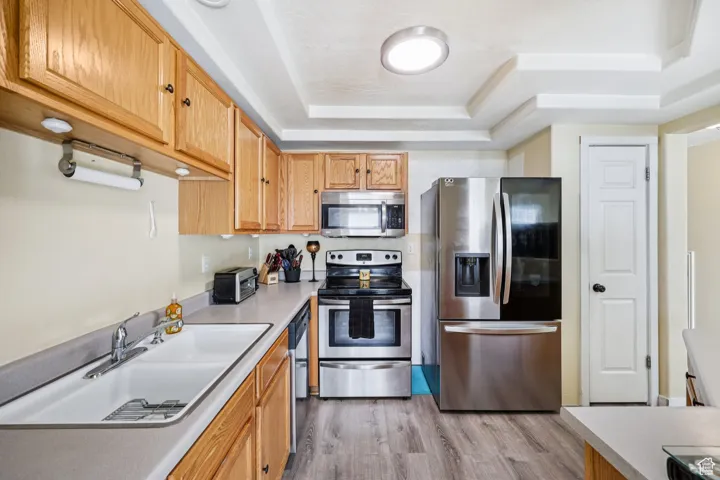 Kitchen featuring stainless steel appliances, light countertops, a raised ceiling, light wood-style floors, and brown cabinetry