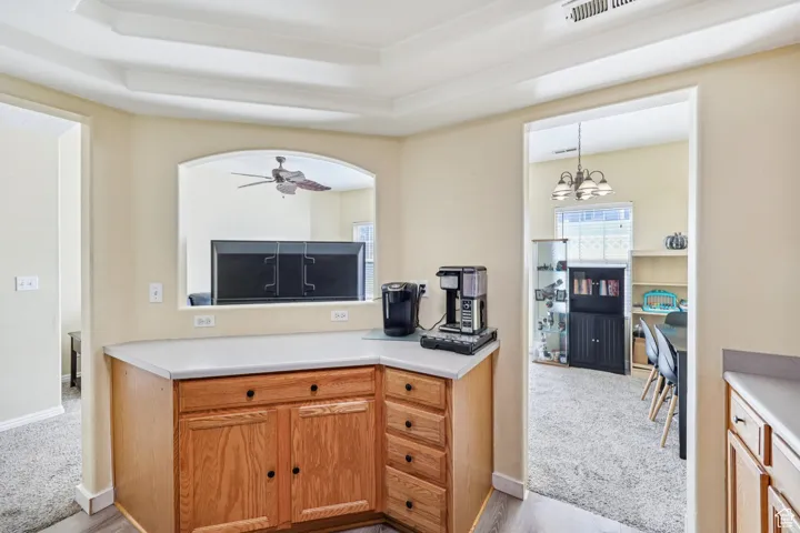 Kitchen with light colored carpet, light countertops, ceiling fan, a chandelier, and a raised ceiling