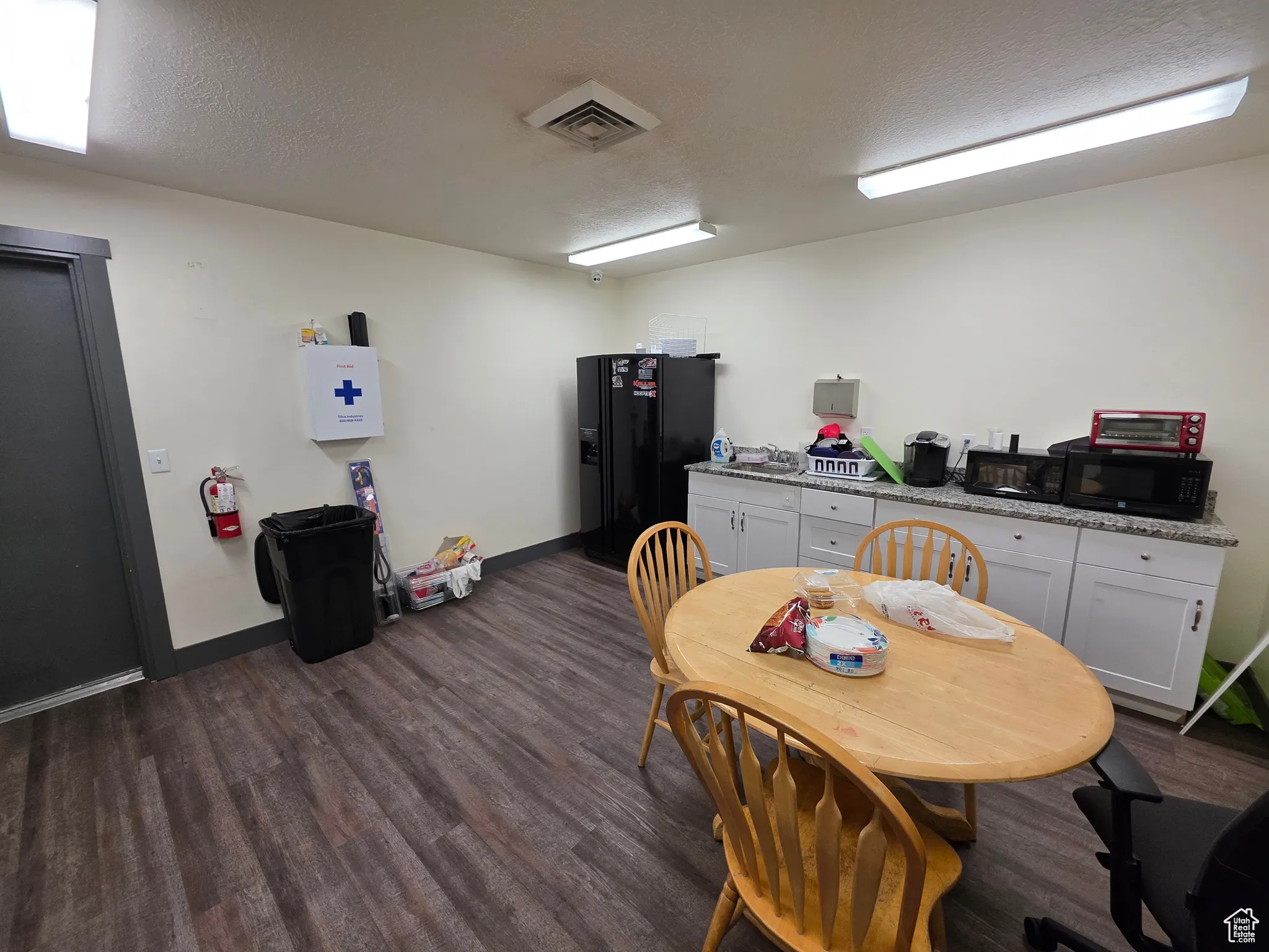 Kitchen with a textured ceiling, black appliances, dark wood-style flooring, light stone countertops, and white cabinetry