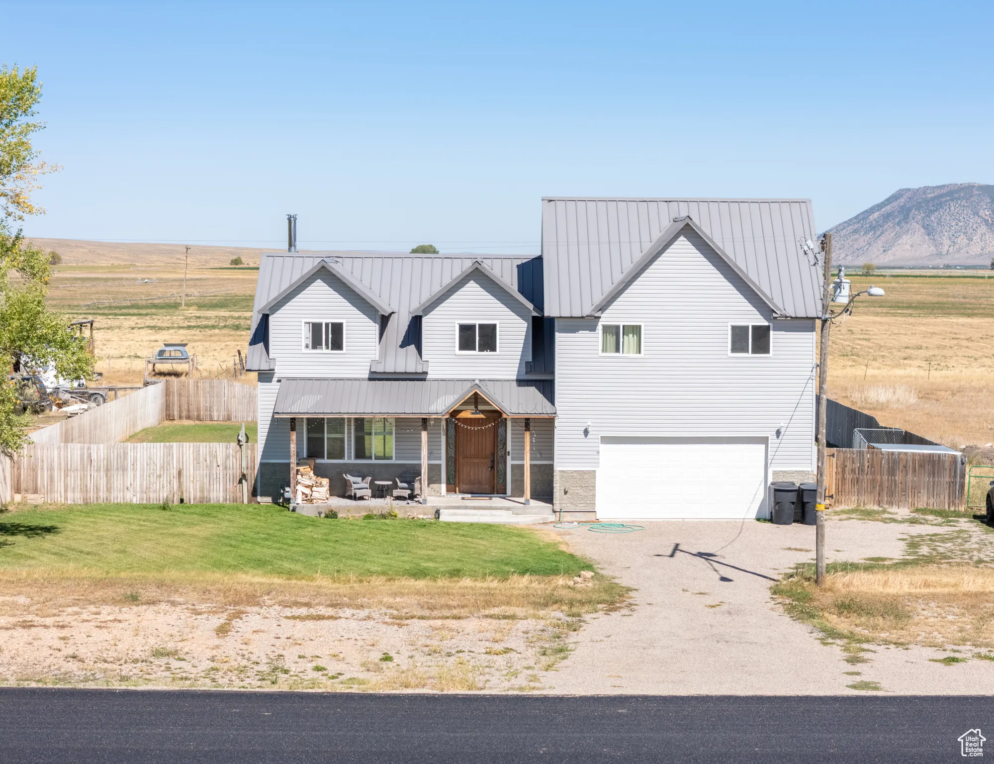 Modern farmhouse style home with dirt driveway, covered porch, a metal roof, a garage, and a view of countryside