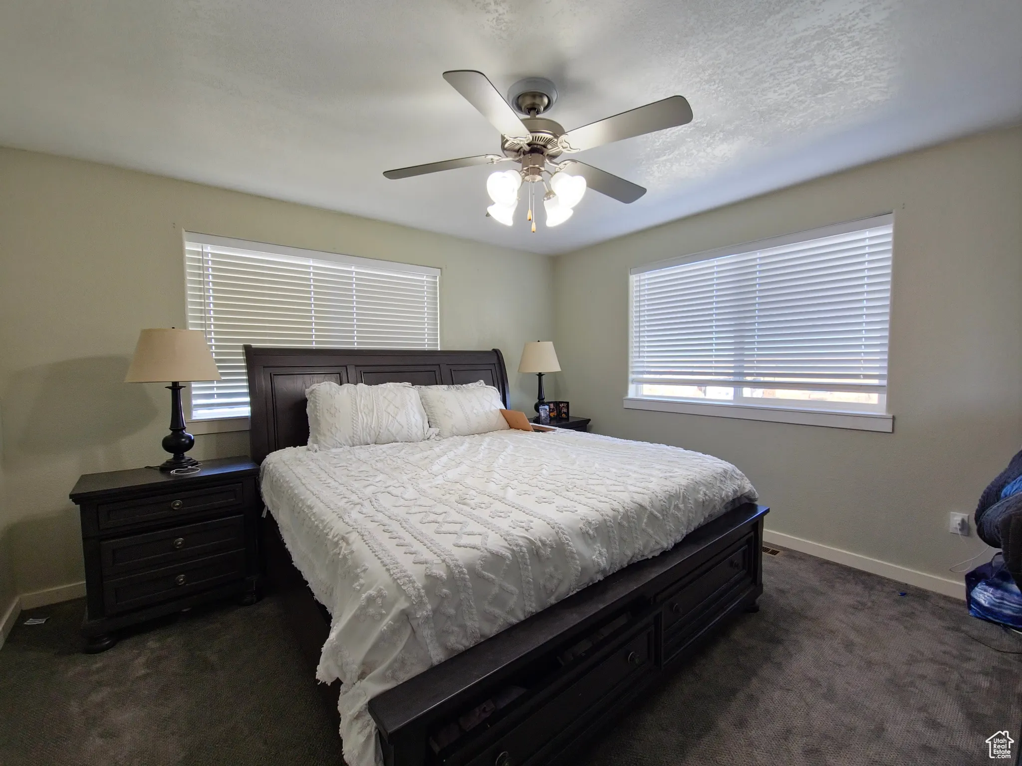 Bedroom with dark carpet, multiple windows, and ceiling fan