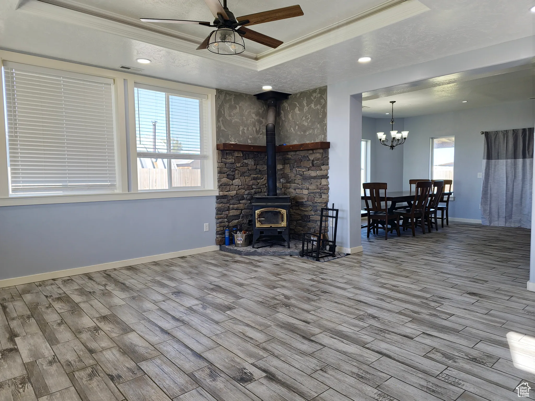 Living room featuring a wood stove, a tray ceiling, wood tiled floors, a ceiling fan, and crown molding