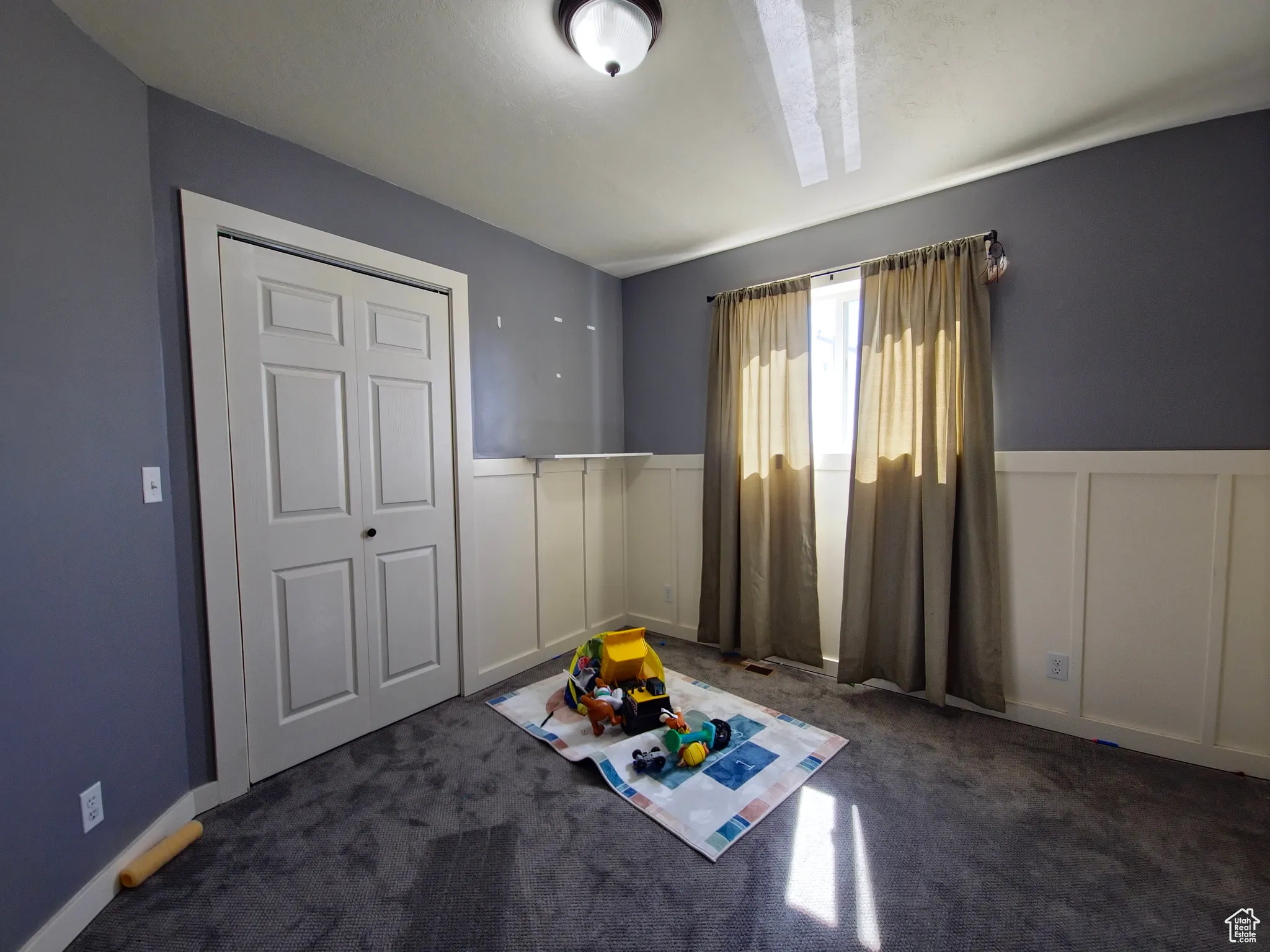 Unfurnished bedroom featuring carpet flooring, a decorative wall, a closet, and a wainscoted wall