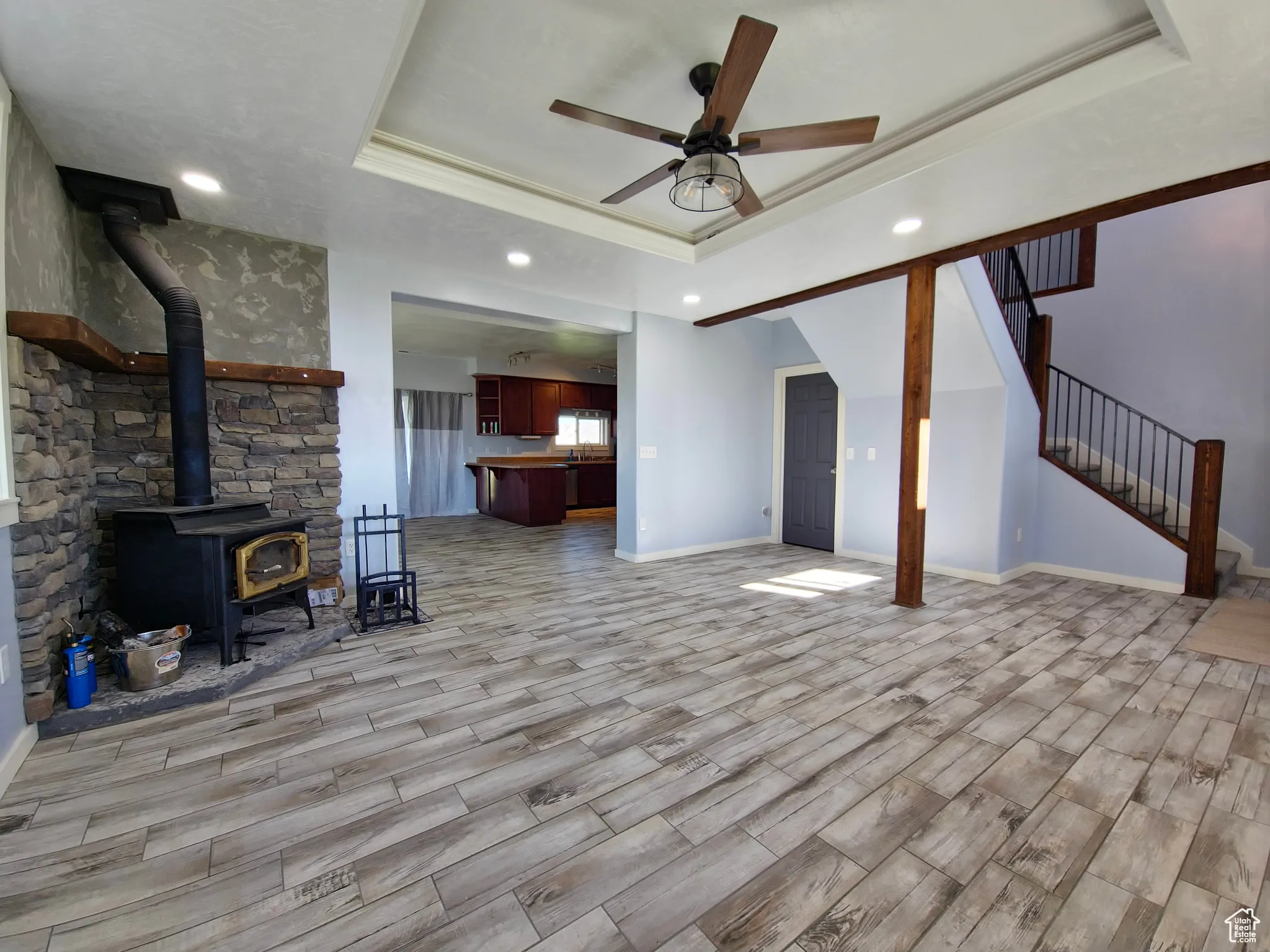 Living room featuring a raised ceiling, a wood stove, wood tiled floors, recessed lighting, and ornamental molding