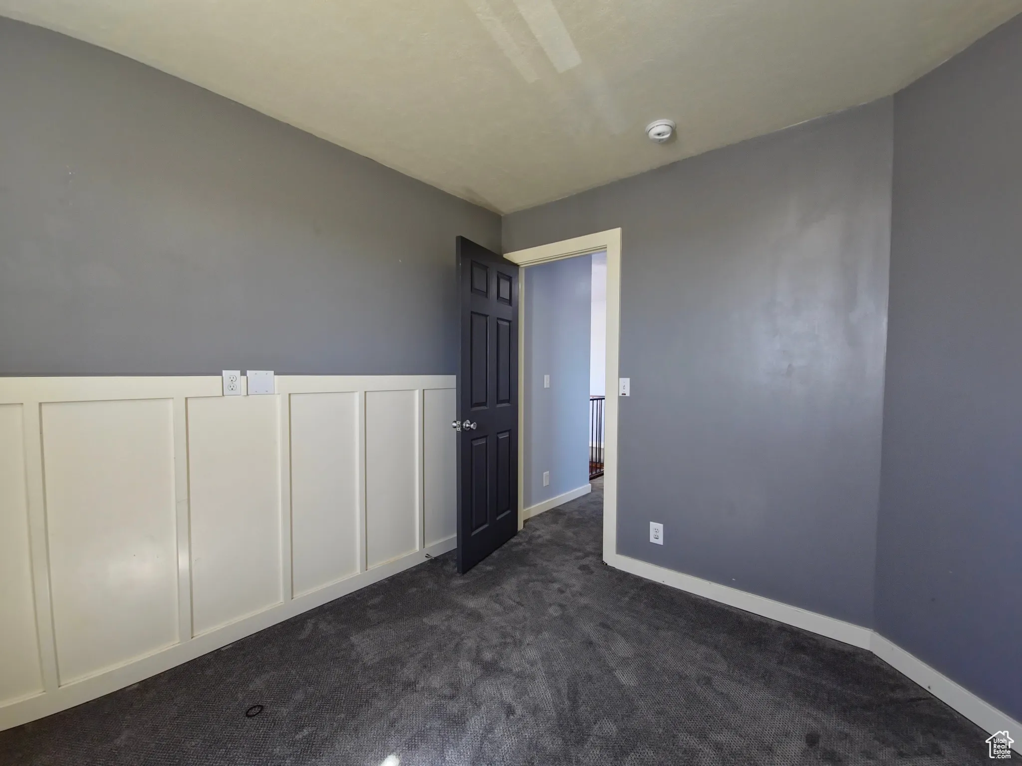 Unfurnished bedroom with dark carpet, a decorative wall, wainscoting, and a ceiling fan