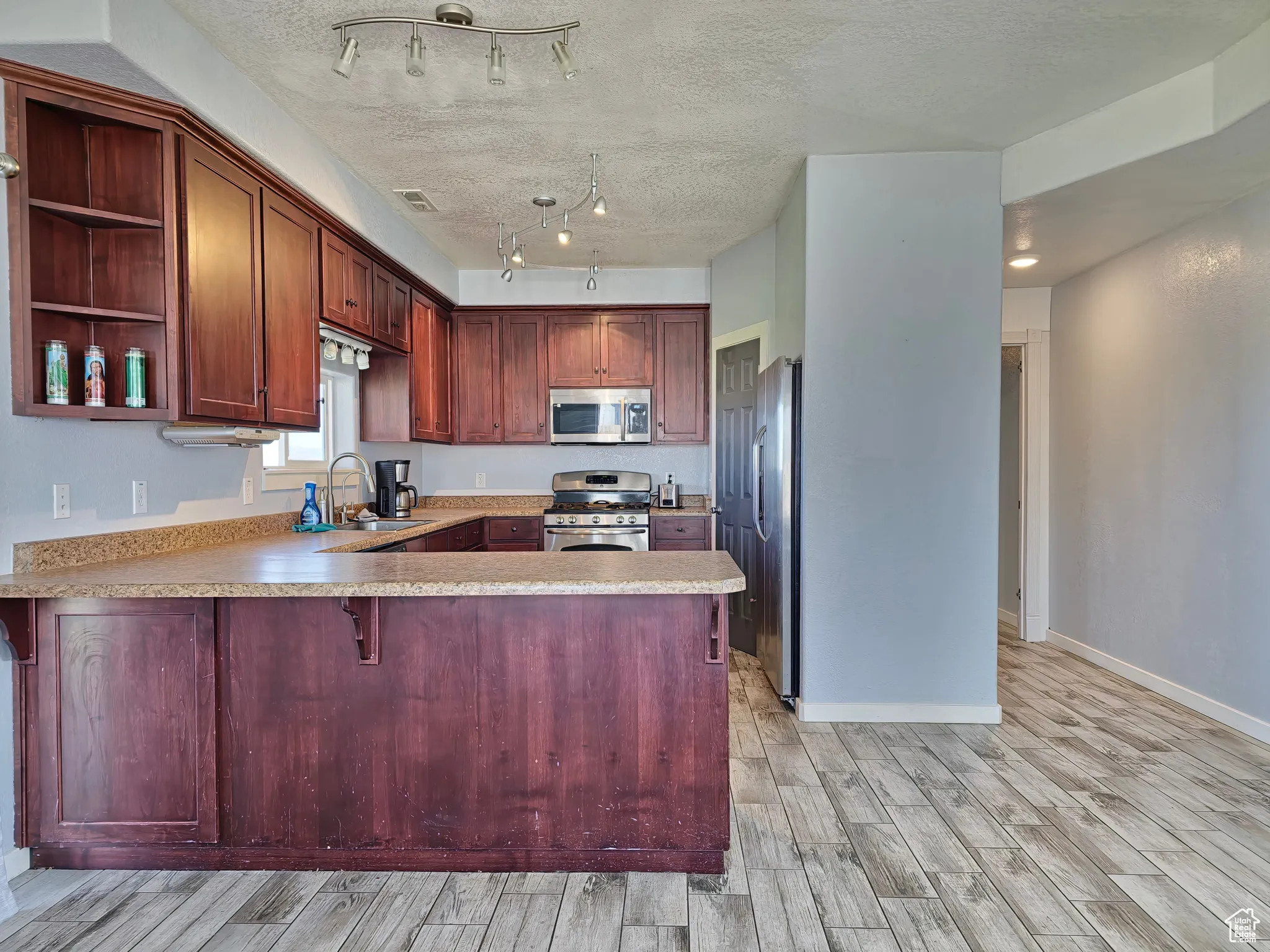Kitchen featuring open shelves, appliances with stainless steel finishes, light countertops, light wood-style floors, and a peninsula