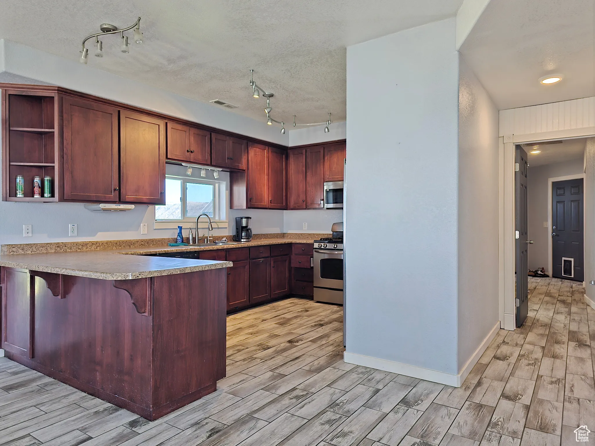 Kitchen featuring a breakfast bar area, open shelves, stainless steel appliances, wood tiled floors, and a textured ceiling