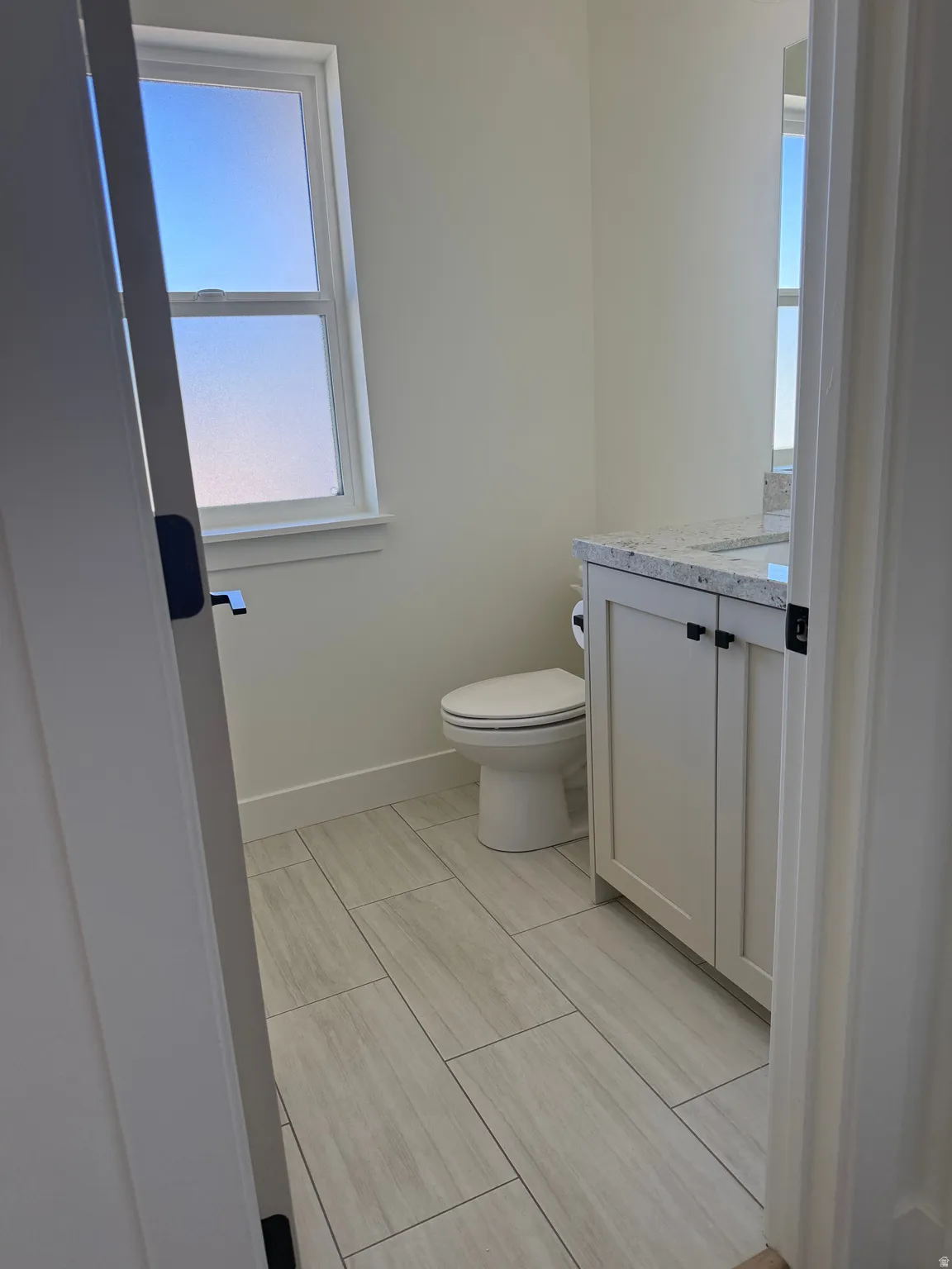 Full bathroom featuring a single window, a white vanity with a speckled countertop, and light-toned rectangular floor tiles