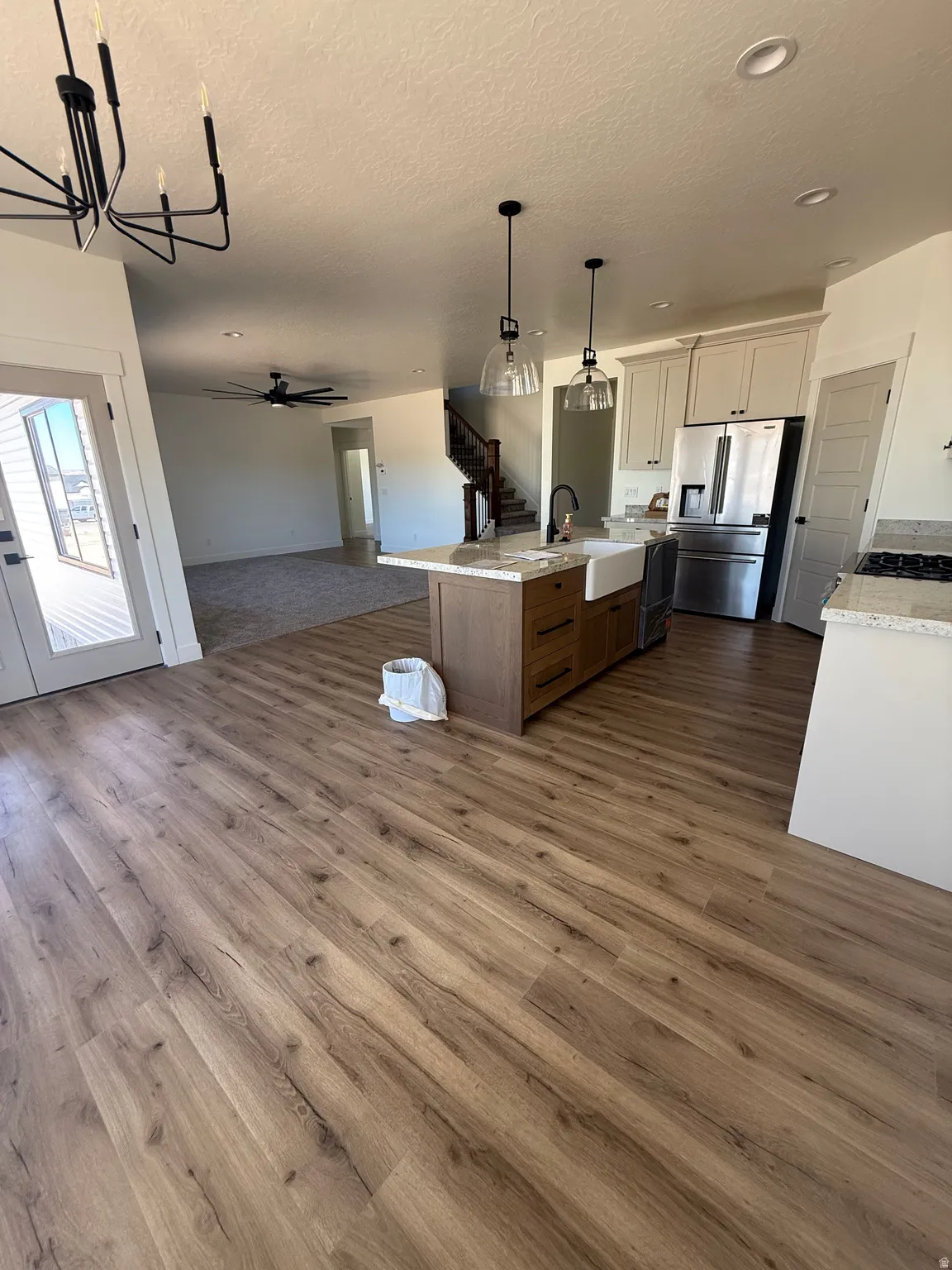 Wood-finish flooring throughout, kitchen island with built-in farmhouse sink, stainless steel appliances, white cabinetry, and recessed lighting