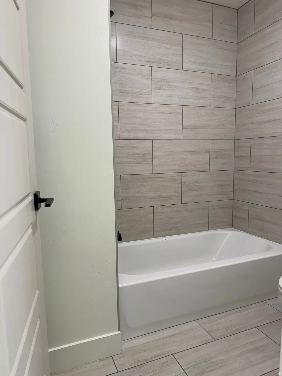 Bathtub with subway tile surround, wood-finish flooring, and matte black fixtures