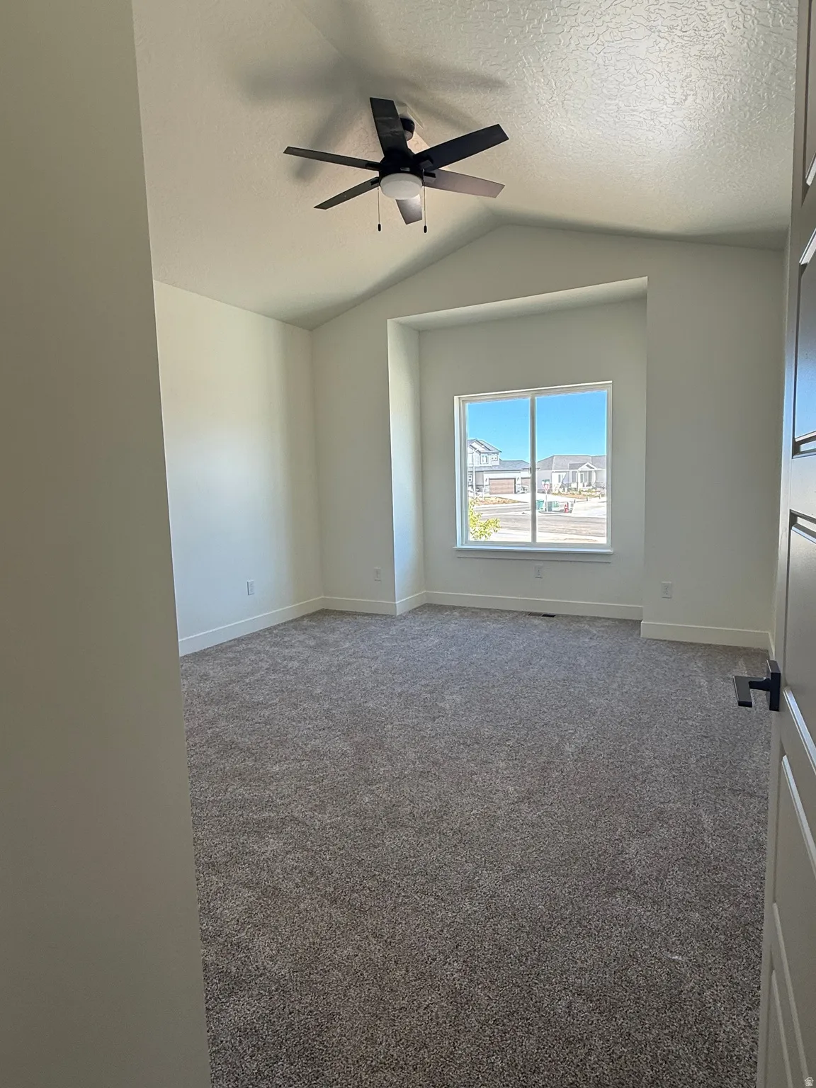 Vaulted ceiling room featuring a ceiling fan with integrated lighting, a large window, and plush carpeting