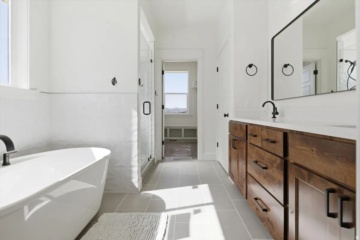 Full bath with vanity, a freestanding tub, a shower stall, light tile patterned flooring, and tile walls