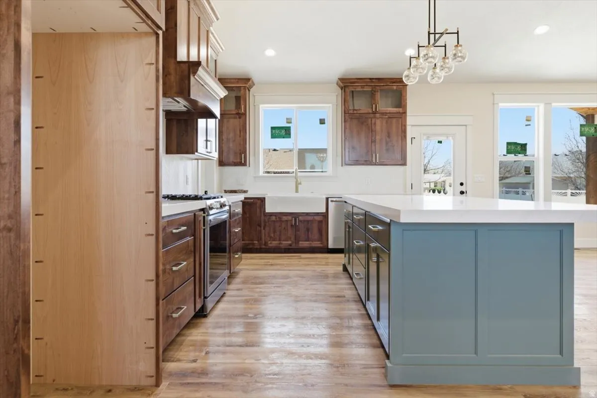 Kitchen with a center island, glass insert cabinets, light wood-style flooring, stainless steel appliances, and decorative light fixtures
