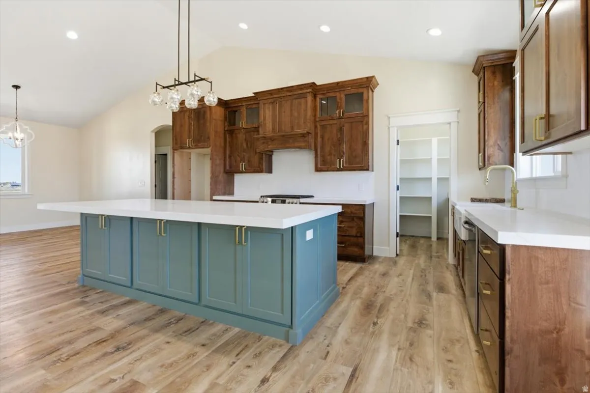Kitchen featuring a spacious island, plenty of natural light, vaulted ceiling, two tone color scheme, and light wood-type flooring