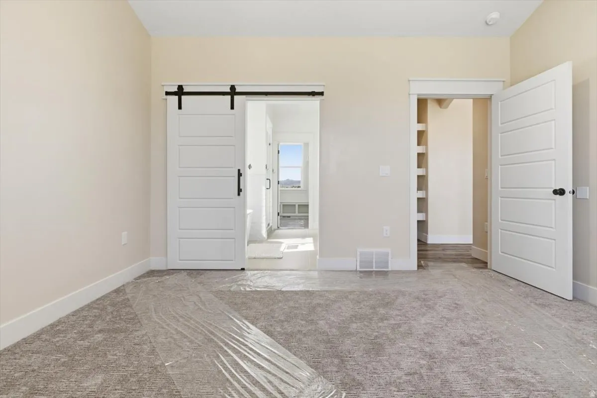 Unfurnished bedroom featuring a barn door and carpet
