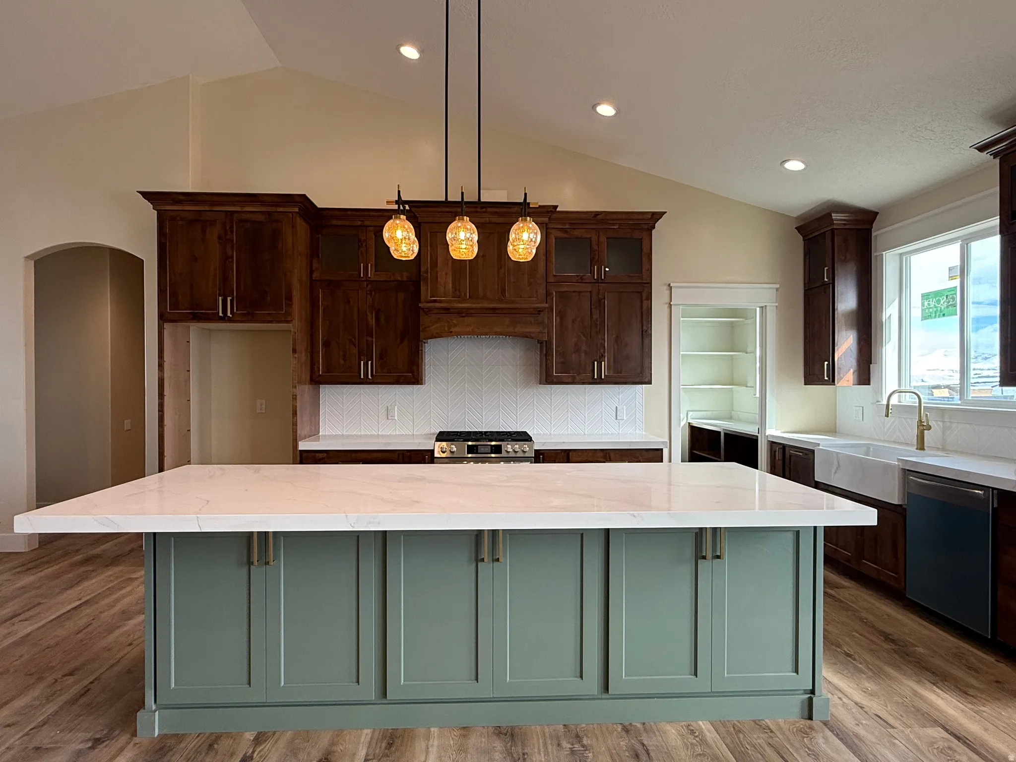 Dual tone kitchen with tasteful backsplash, decorative light fixtures, stainless steel appliances, light stone countertops, and vaulted ceiling