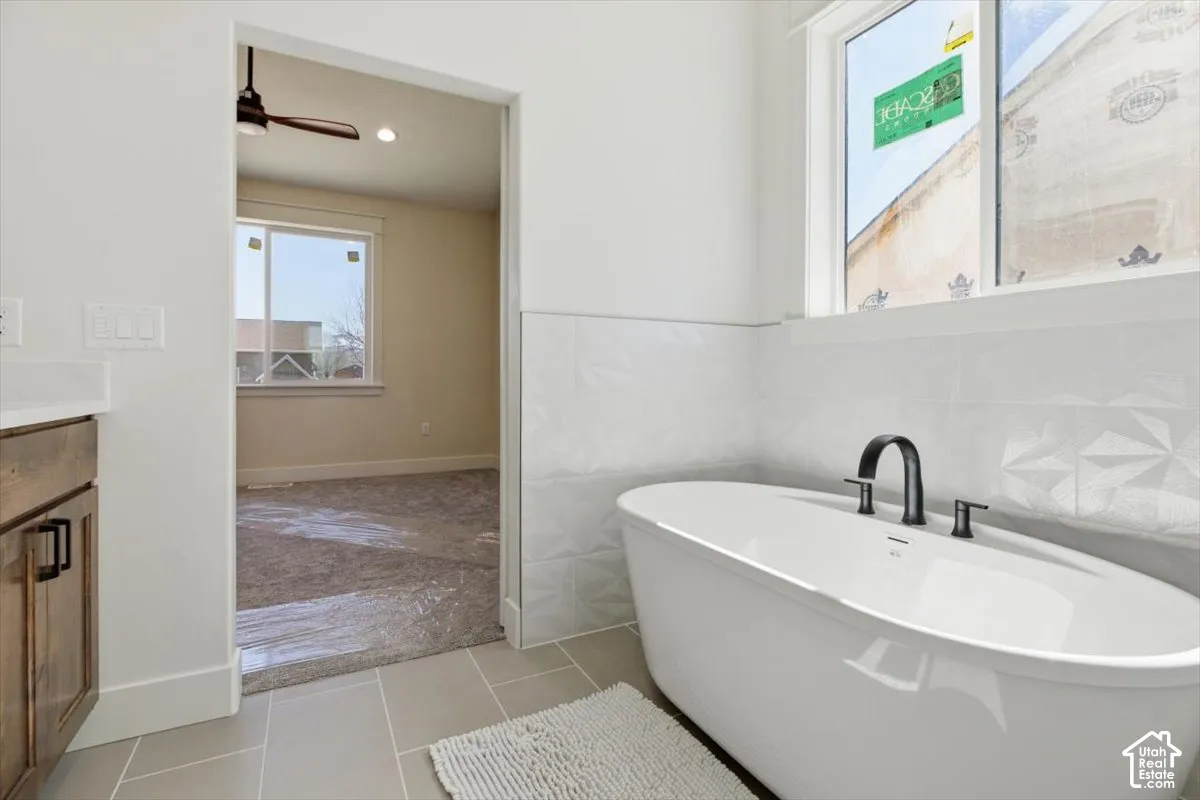 Bathroom featuring tile walls, a soaking tub, vanity, light tile patterned flooring, and ceiling fan