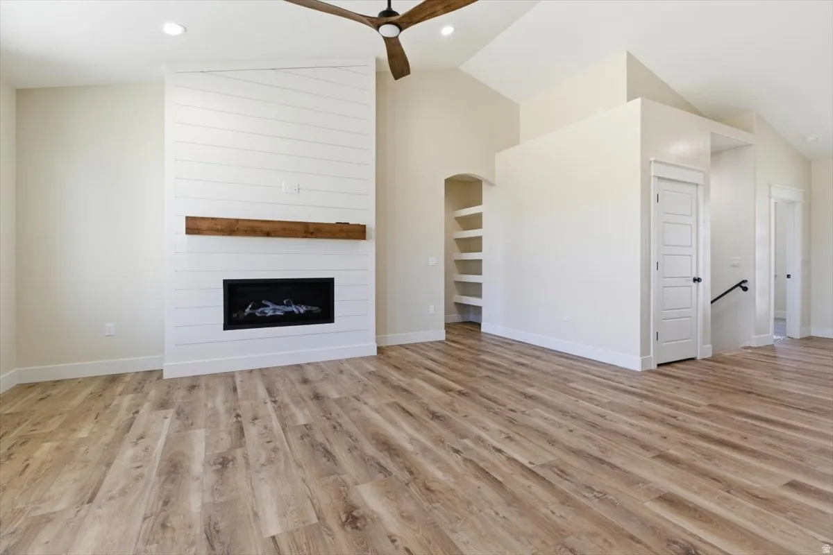 Unfurnished living room featuring vaulted ceiling, light wood-style floors, recessed lighting, a fireplace, and ceiling fan