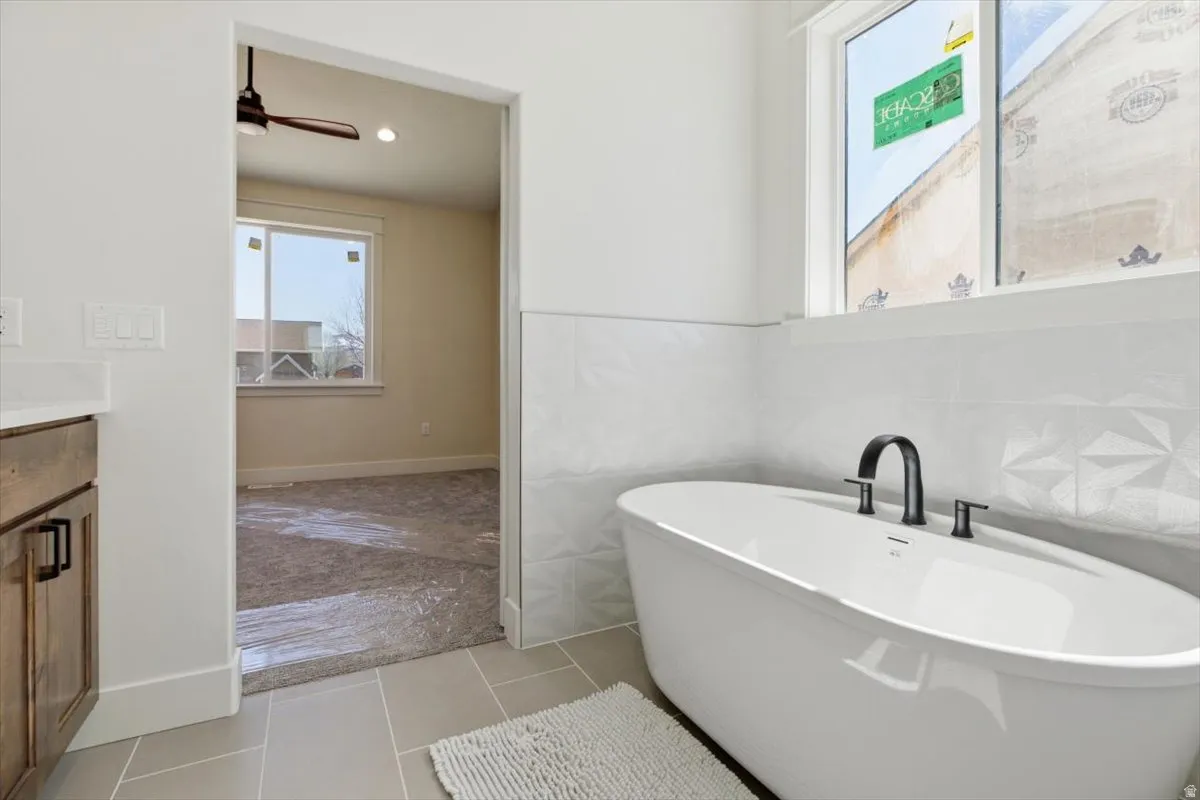 Bathroom featuring tile walls, a soaking tub, vanity, light tile patterned flooring, and ceiling fan