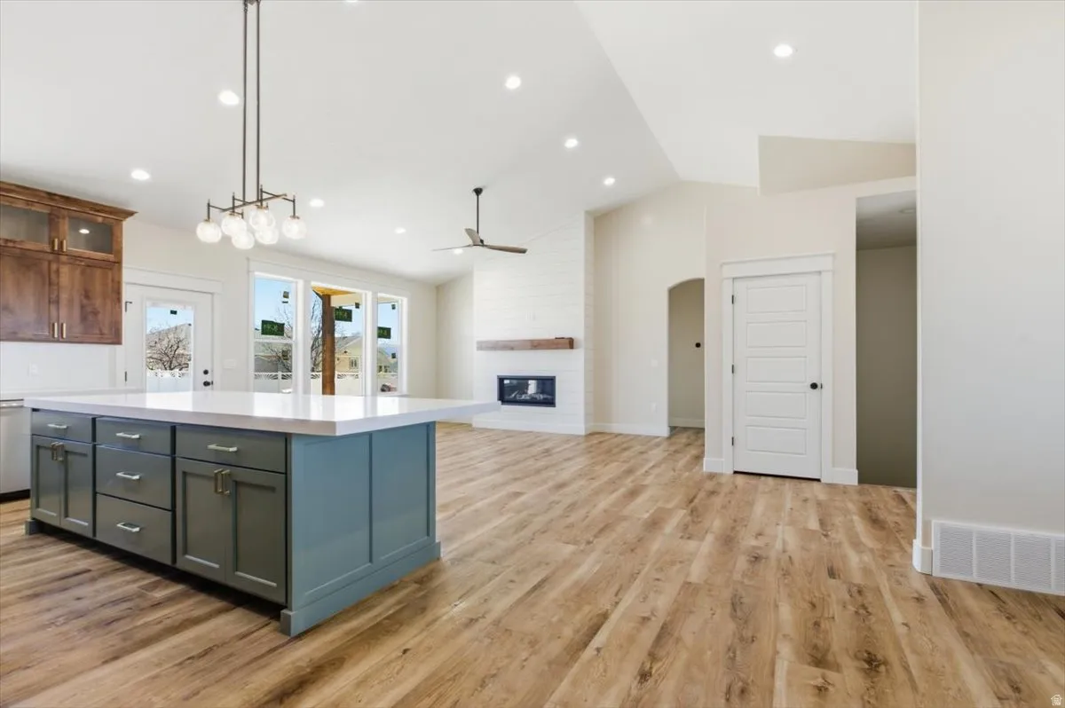 Two tone kitchen with vaulted ceiling, decorative light fixtures, open floor plan, a kitchen island, and a fireplace