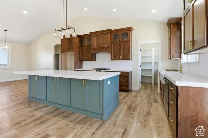 Kitchen featuring a spacious island, plenty of natural light, vaulted ceiling, two tone color scheme, and light wood-type flooring