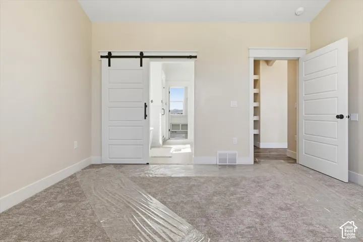 Unfurnished bedroom featuring a barn door and carpet