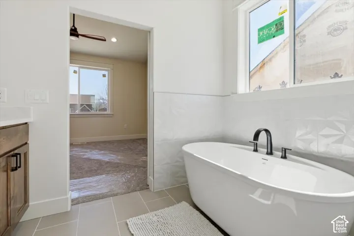 Bathroom featuring tile walls, a soaking tub, vanity, light tile patterned flooring, and ceiling fan