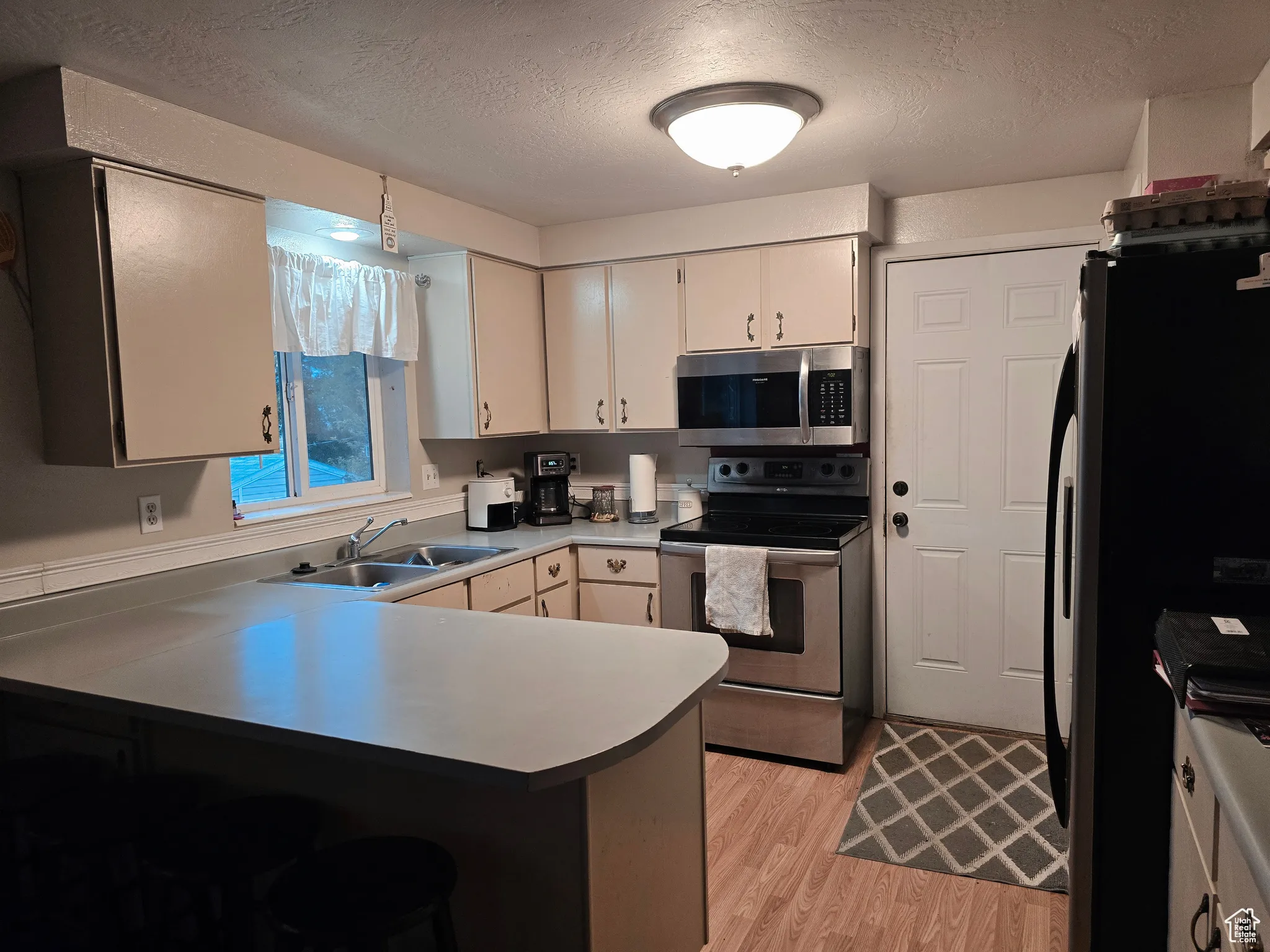 Kitchen with a textured ceiling, stainless steel appliances, a peninsula, light wood-style flooring, and a kitchen bar
