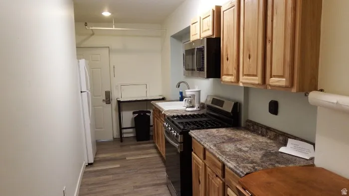 Kitchen with appliances with stainless steel finishes, dark wood finished floors, dark stone counters, and brown cabinets