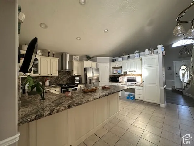 Kitchen featuring decorative backsplash, stainless steel appliances, recessed lighting, a peninsula, and wall chimney range hood