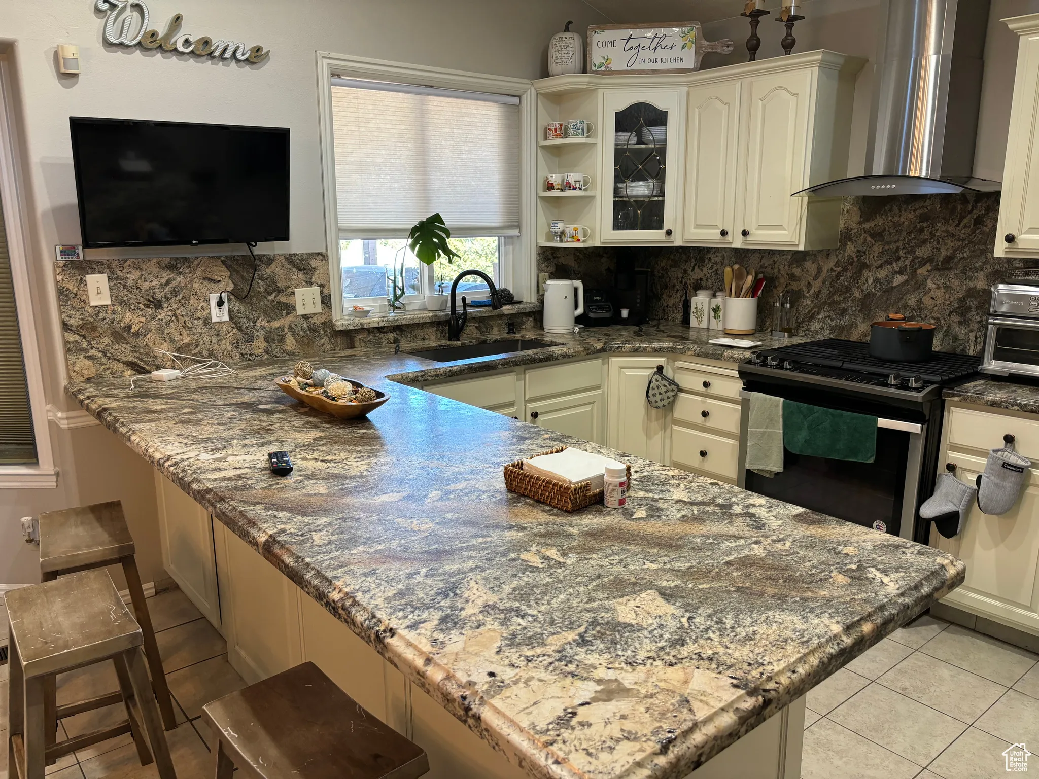 Kitchen featuring wall chimney exhaust hood, backsplash, dark stone counters, and stainless steel gas range oven