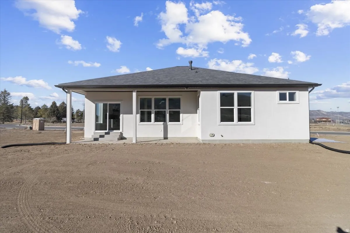 Rear view of property featuring a patio, a shingled roof, and stucco siding