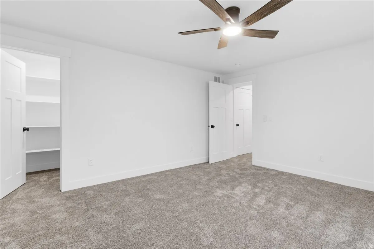Unfurnished bedroom featuring carpet floors, a walk in closet, and a ceiling fan